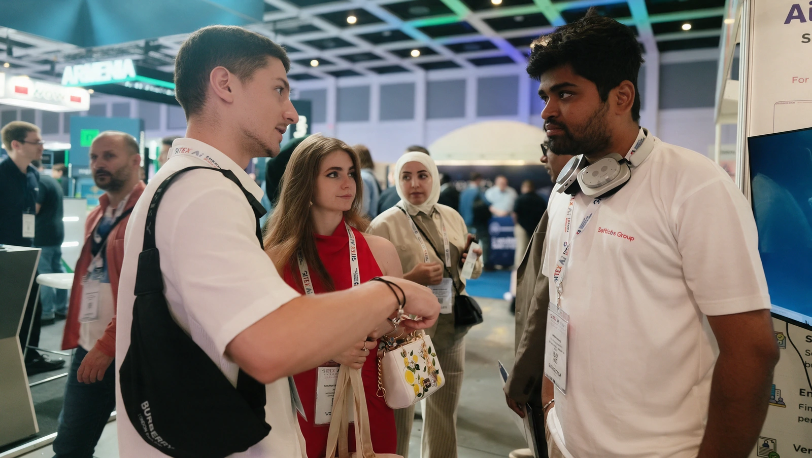A Softlabs representative talking with visitors in a busy exhibition hall.